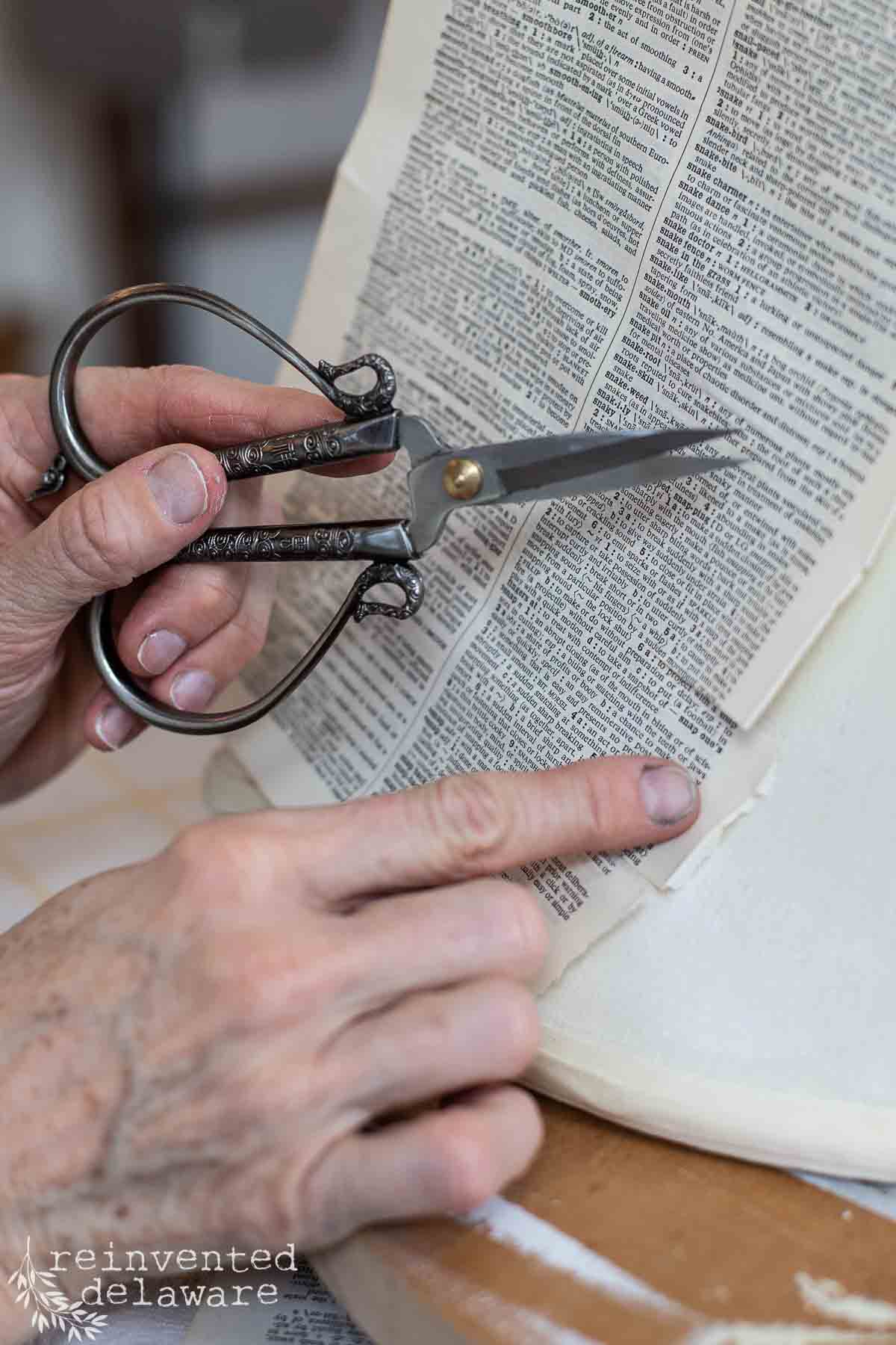 Lady using Mod podge to decoupage dictionary pages to an old lampshade and using scissors to cut the paper to fit.
