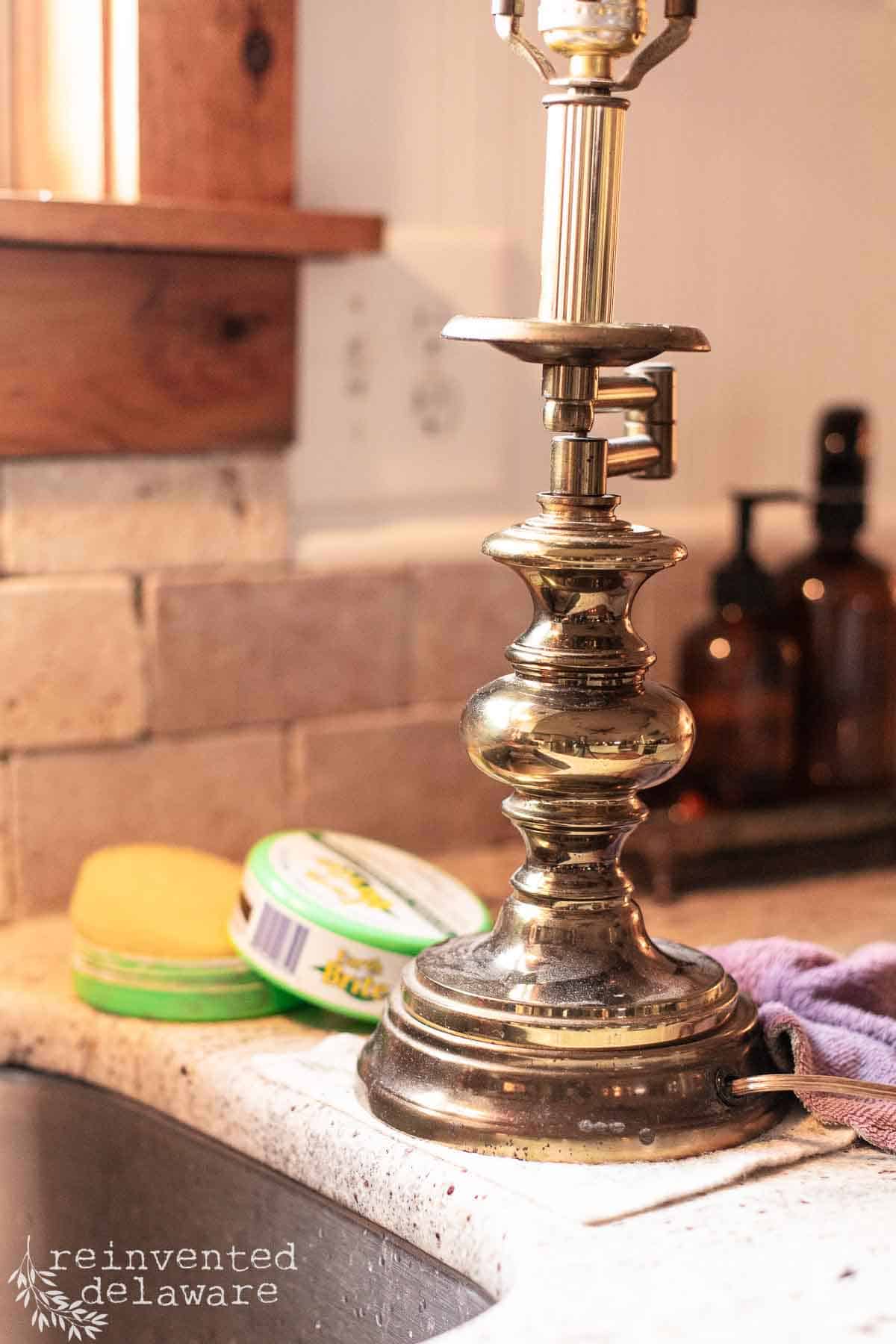 An old brass lamp sitting next to a sink ready to be polished with Earth Brite cleaner for a thrift store lamp makeover project.