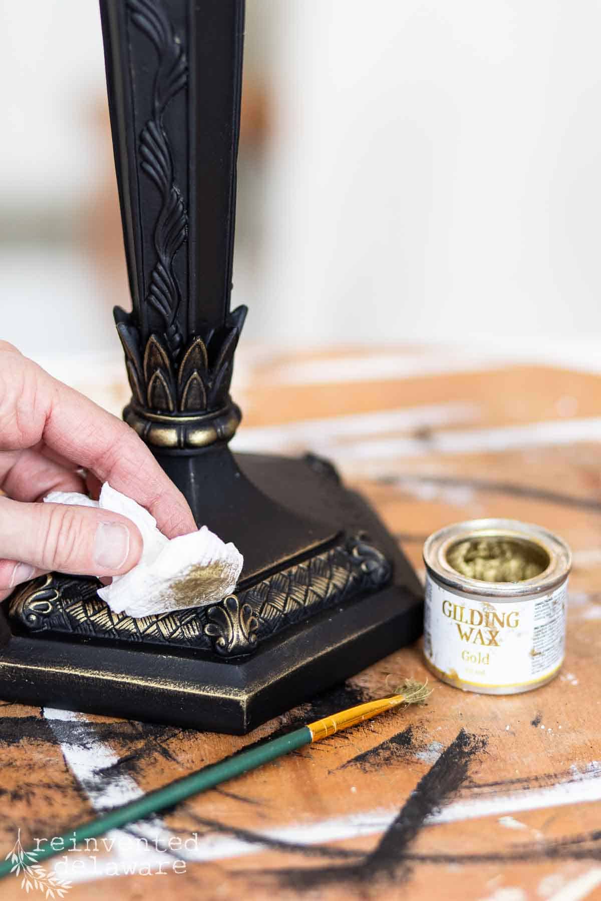 Lady applying gold gilding wax to black painted lamp base for a thrift store lamp makeover project.