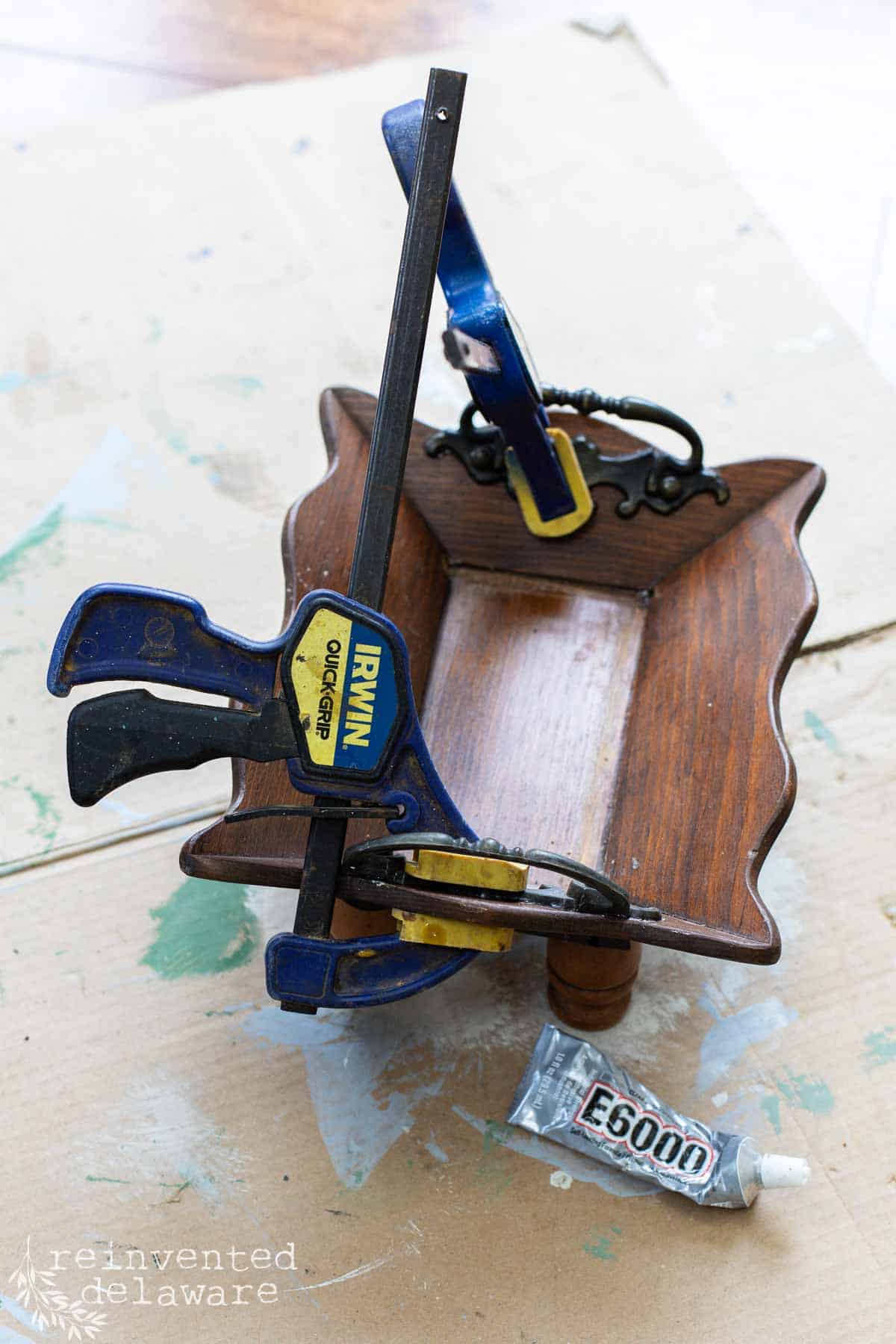 lady glueing on metal handles onto wooden tray for a flea market flip upcycle project. Clamps hold onto the metal handles.