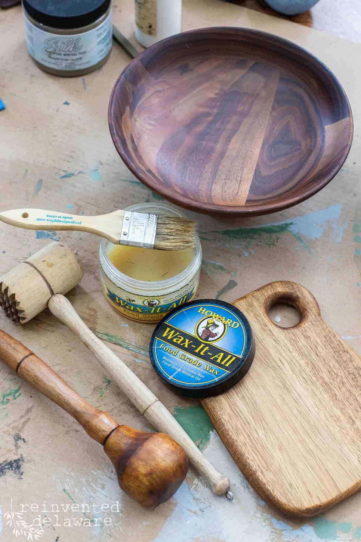 pile of wooden thrift store finds including cutting boards, wooden bowl and utensils along with can of Wax it All food safe protector