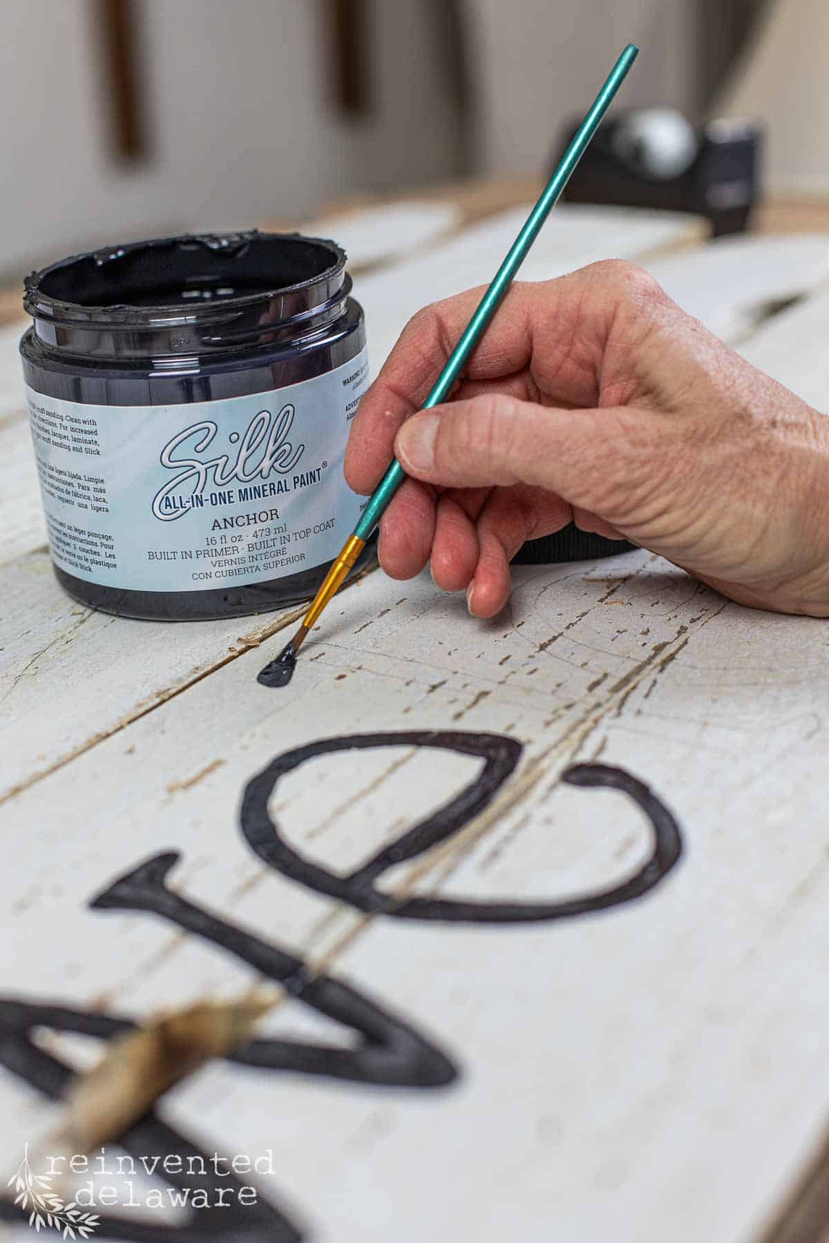 lady painting the word welcome on a diy welcome sign project