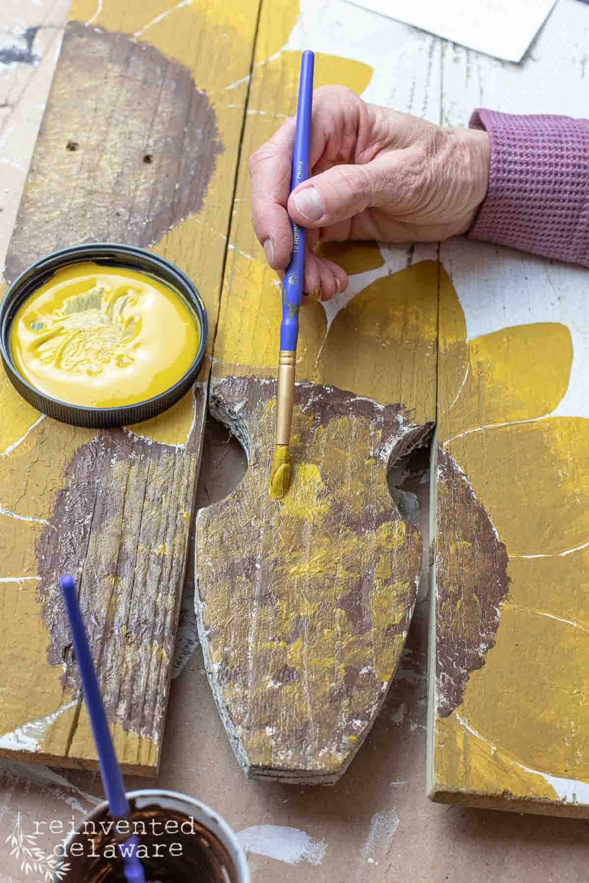 lady painting a diy scrap wood welcome sign with sunflowers