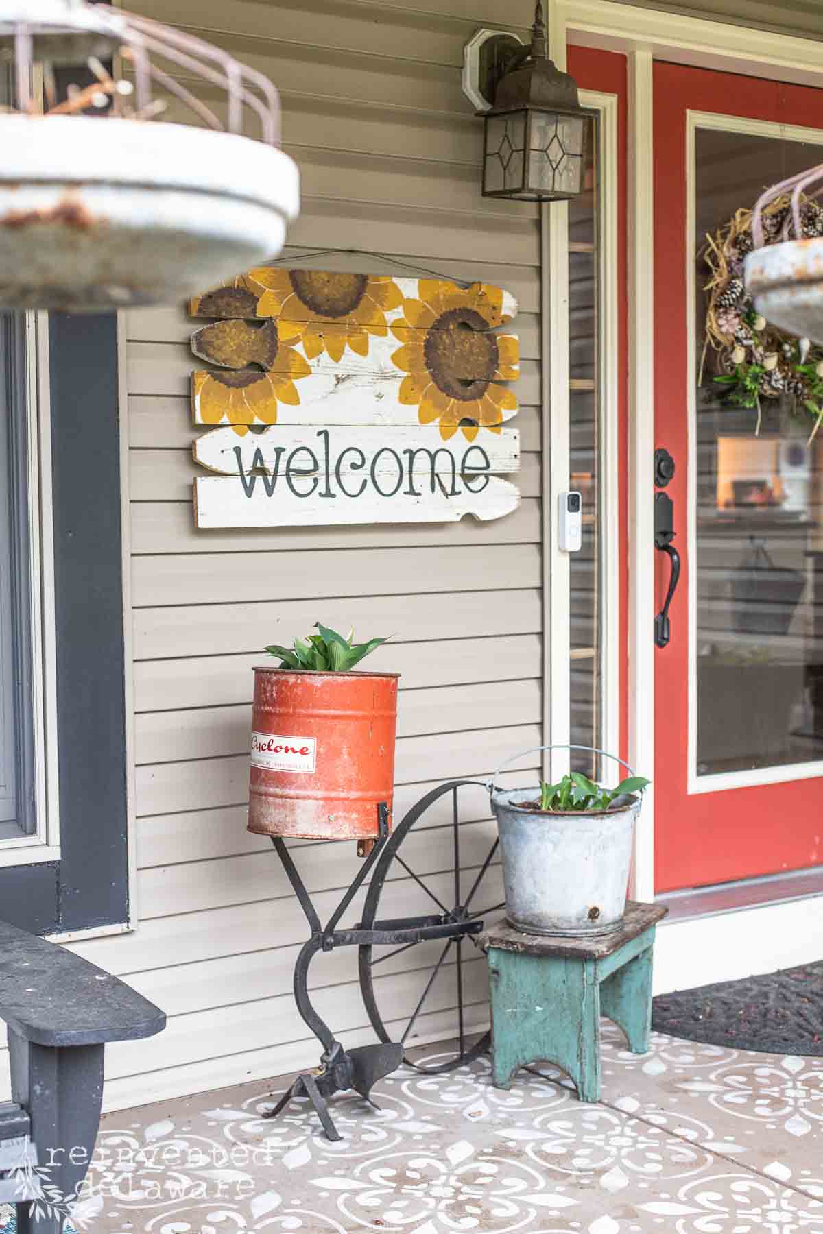 Front porch showing a welcome sign with sunflowers, a planter and a front door