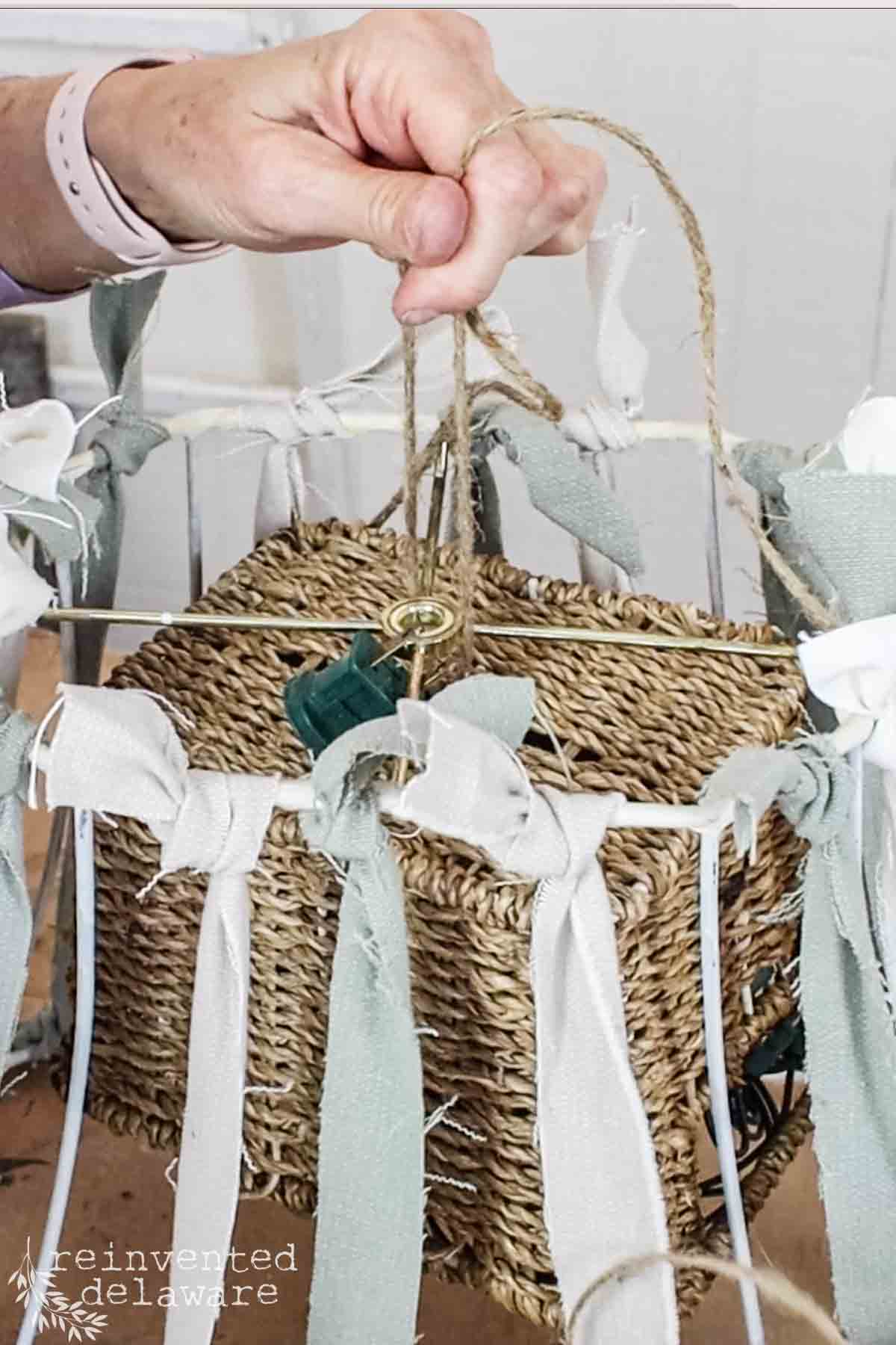 a lady tieing a basket filled with string lights for a hanging lampshade pendant light makeover from an old lampshade