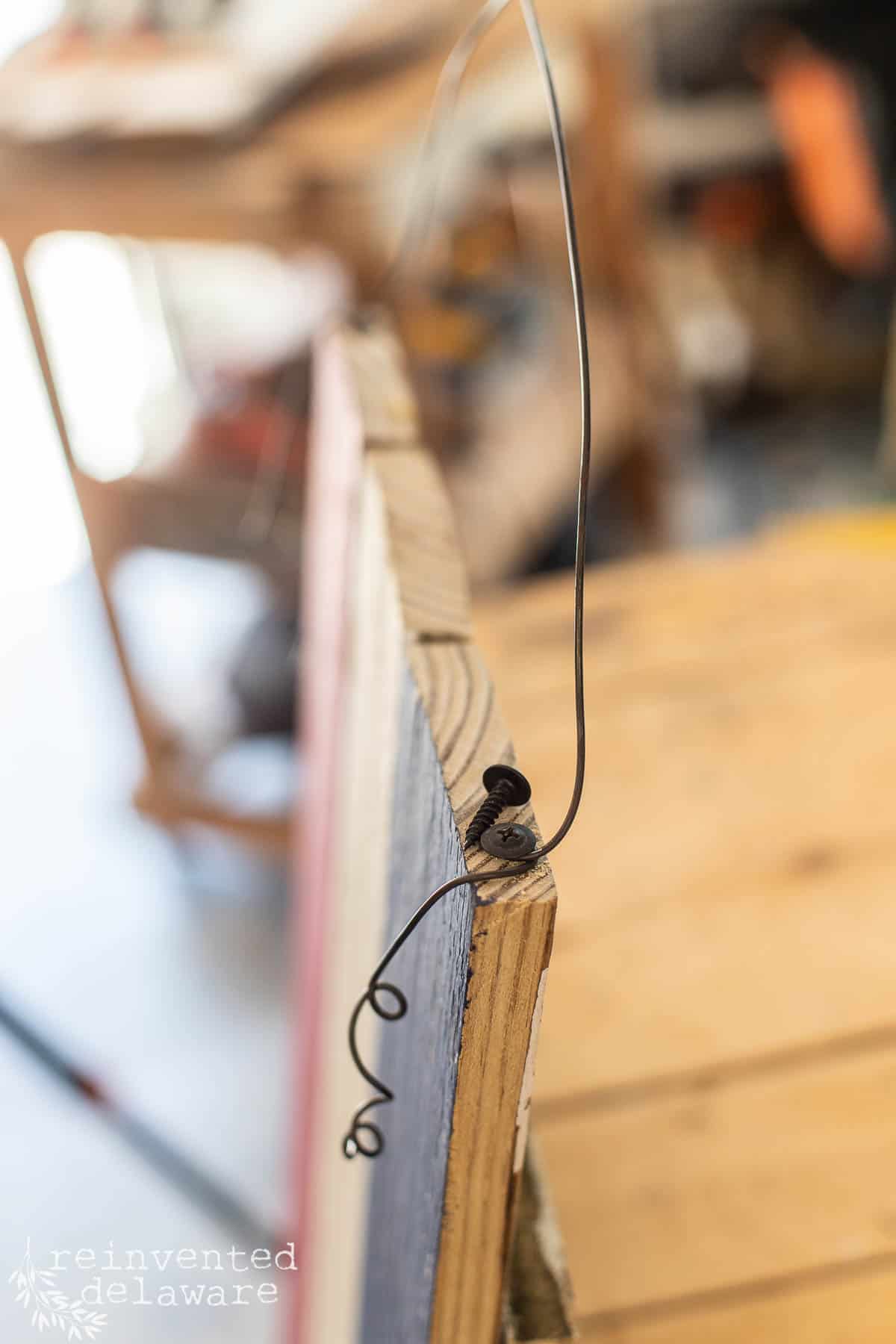 Detail shot showing heavy wire and a screw used to hang a diy wooden flag for decor.
