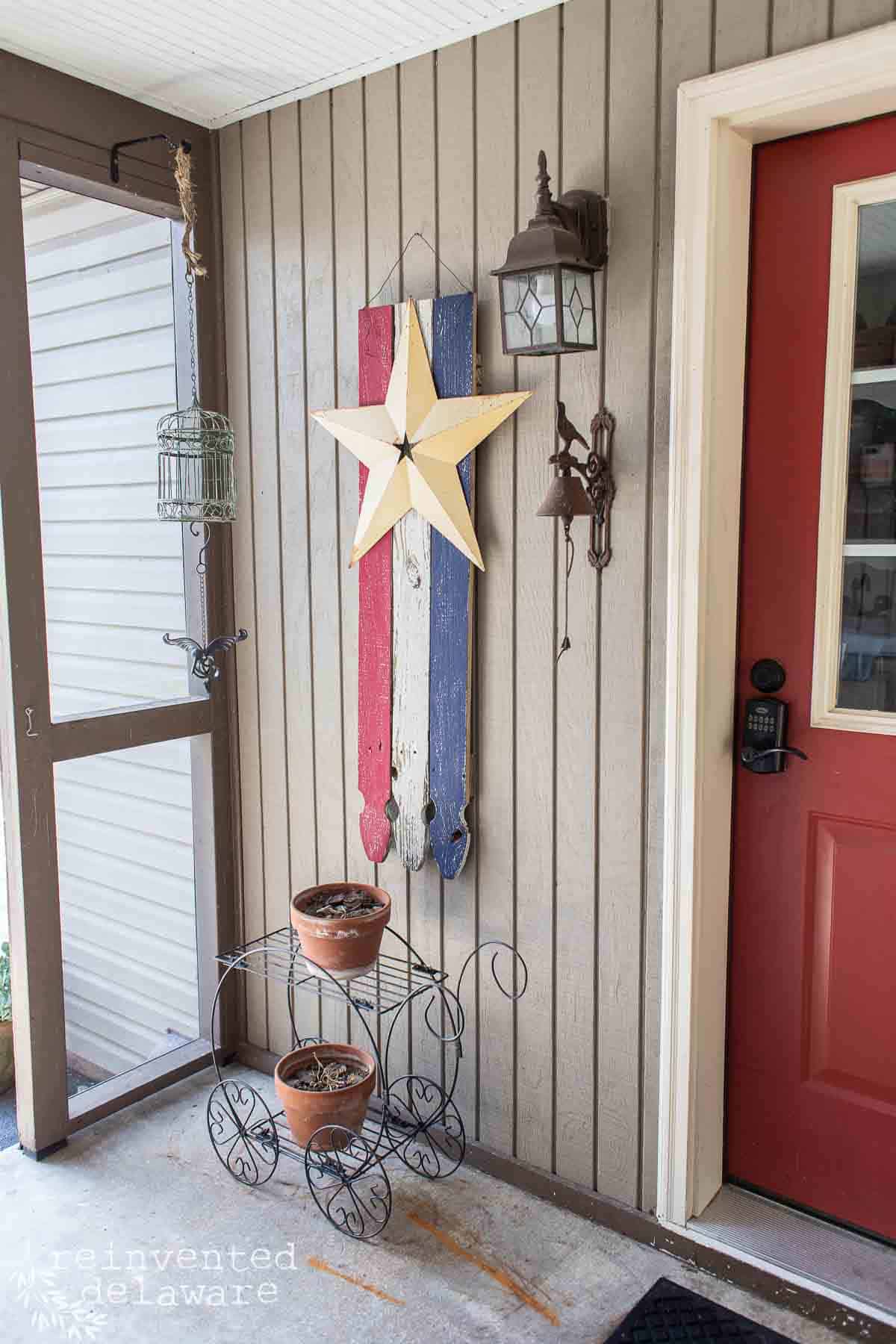 A DIY wood flag made with reclaimed fence picket boards hanging on a back porch near the back door.
