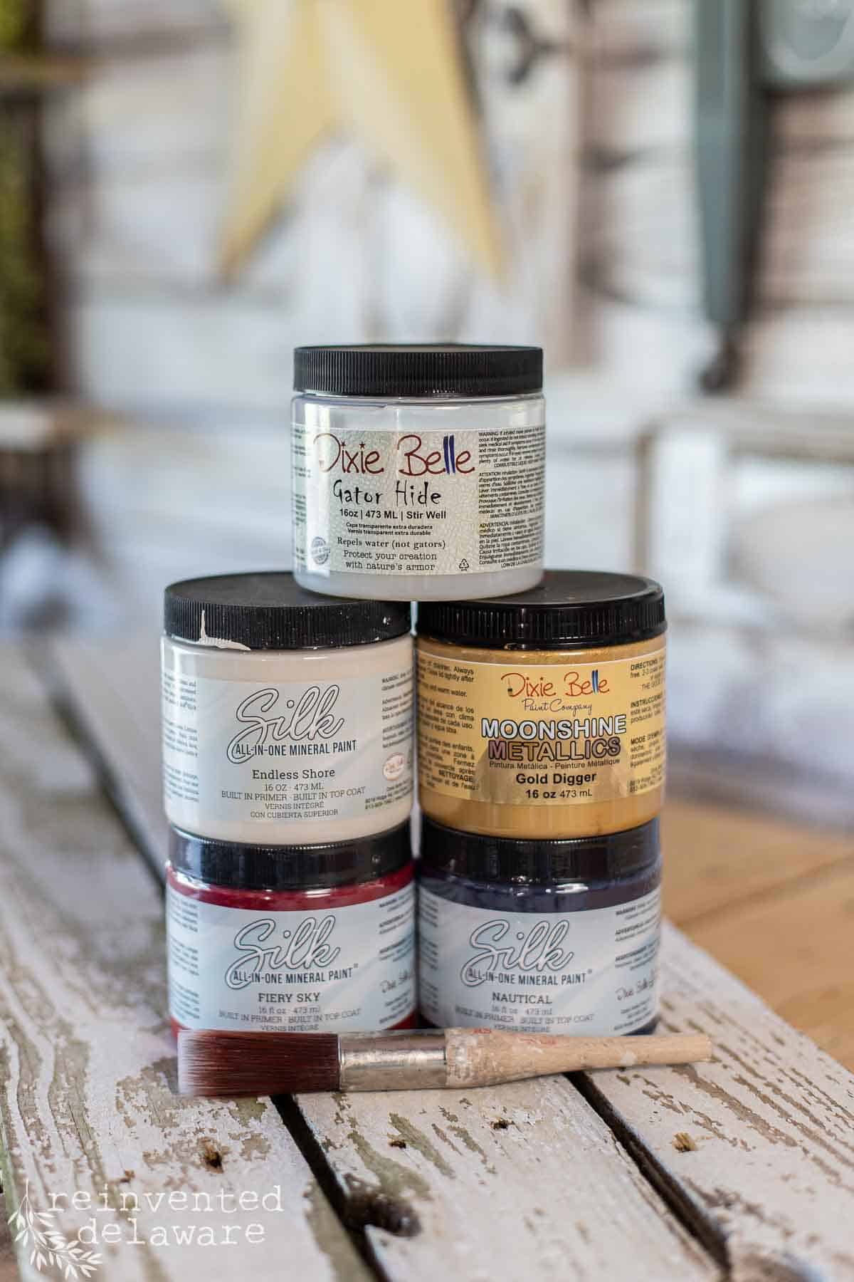 A stack of paint jars in American flag colors to make a DIY wooden sign.