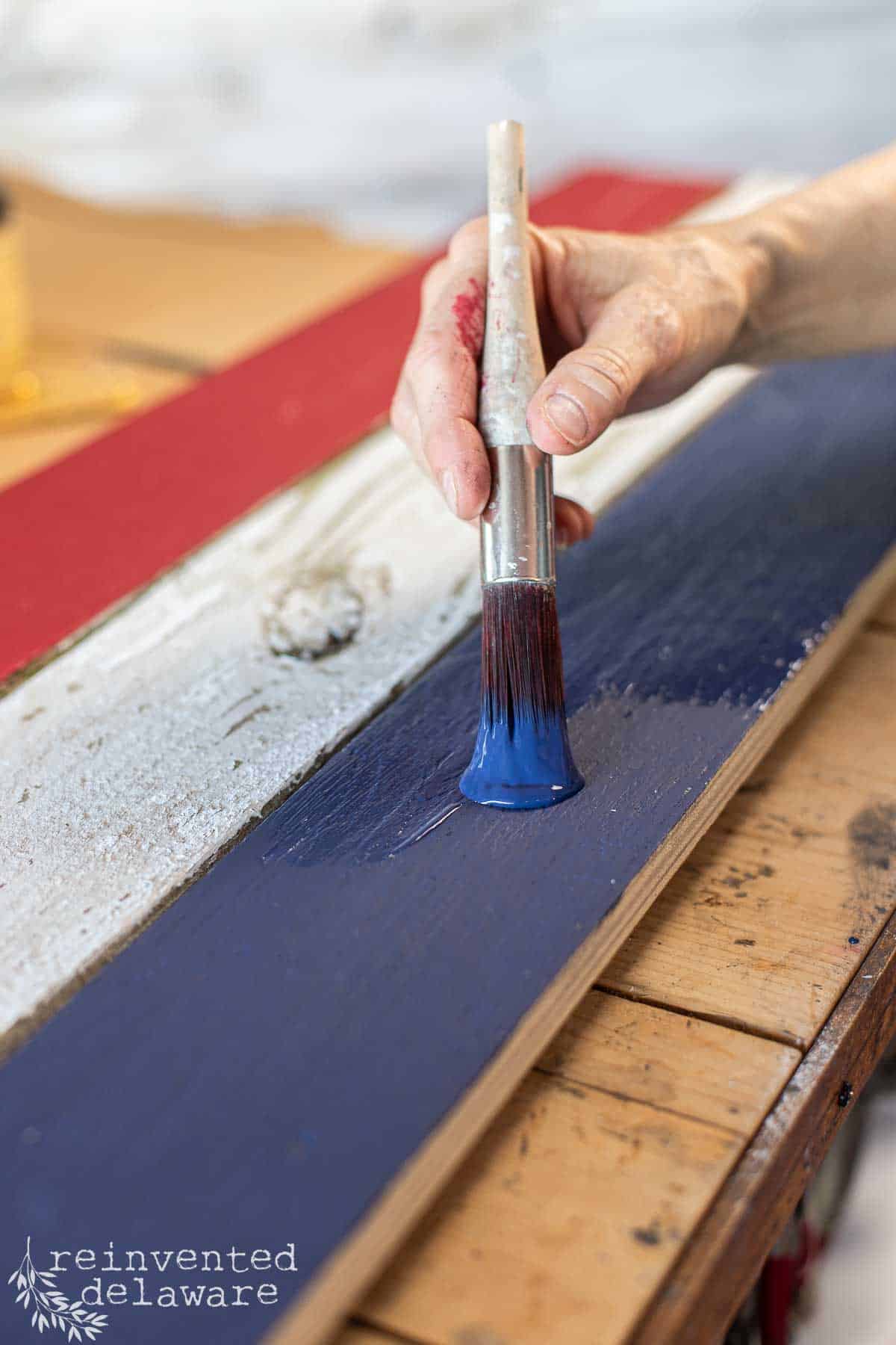 A lady painting fence boards in red, white and blue to create a rustic wood American flag.