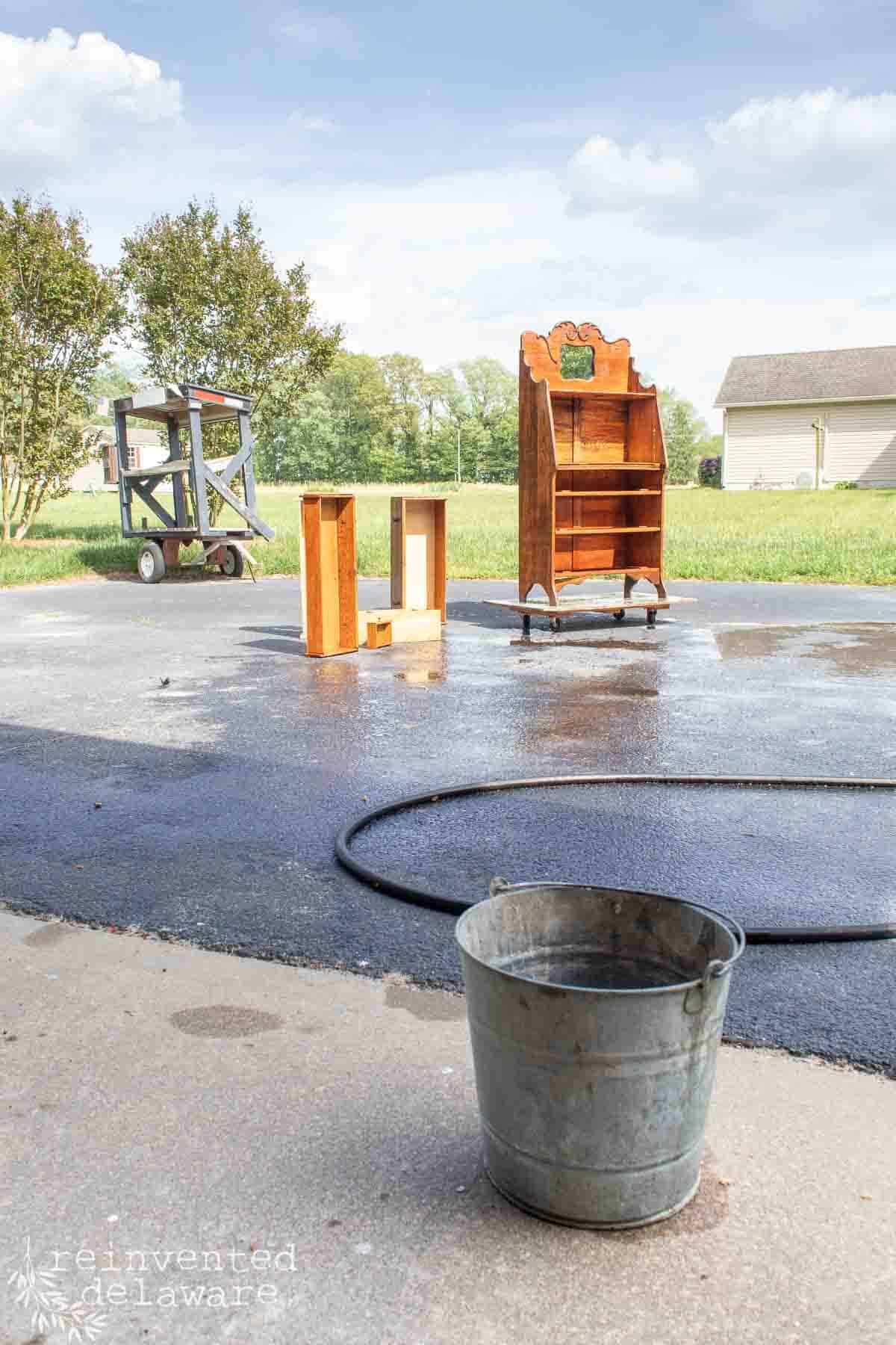 Old piece of oak furniture sitting in the driveway on a sunny day ready to be washed with a bucket of hot soapy water.