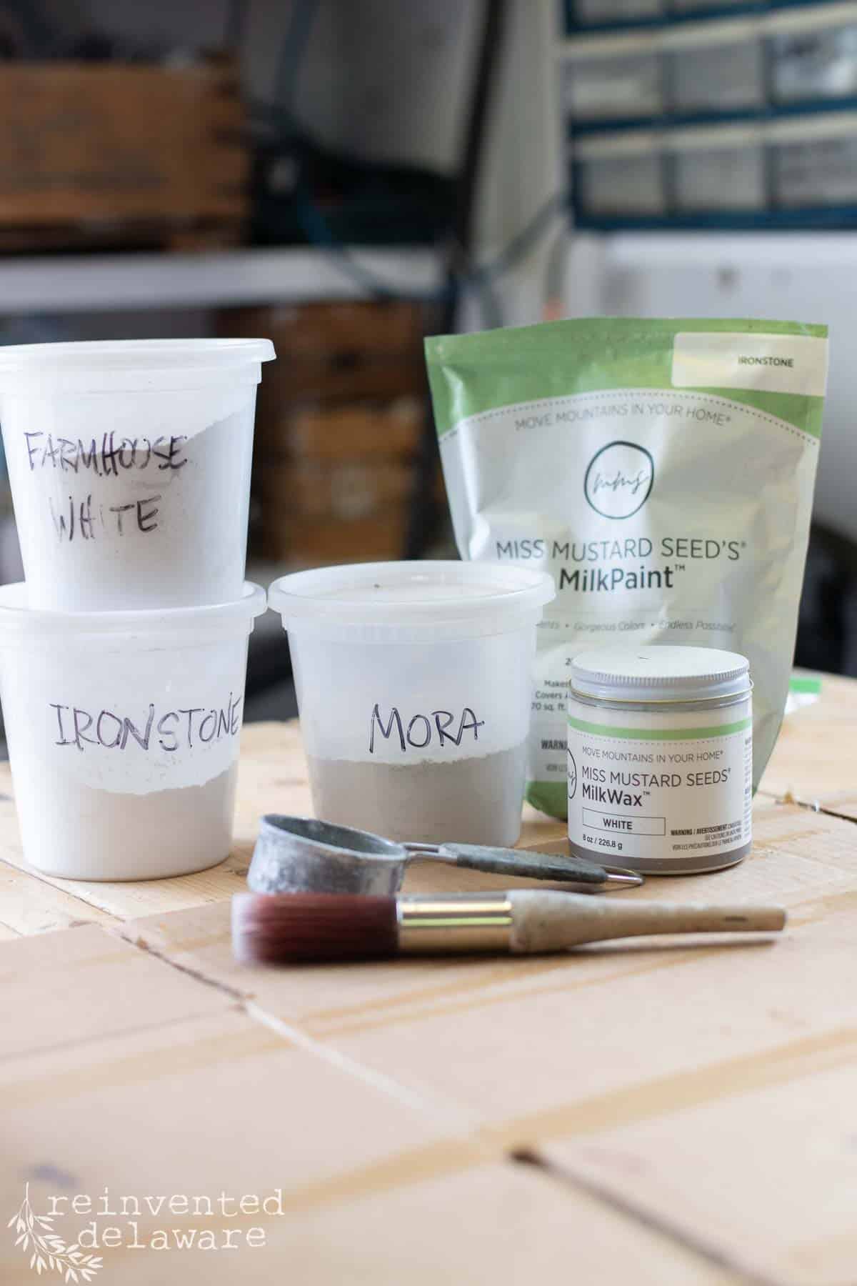 Containers of dry milk pain powder used for a whitewashed furniture makeover technique.