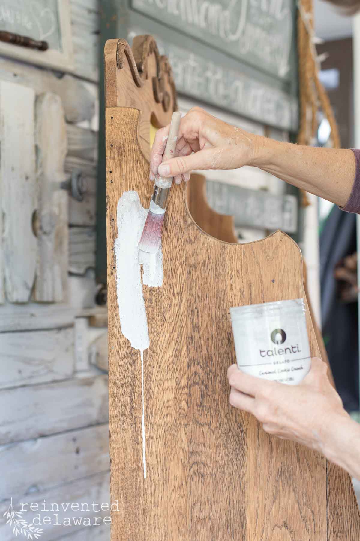Lady applying milk paint to an antique secretary desk as she demonstrates a DIY whitewashing technique.
