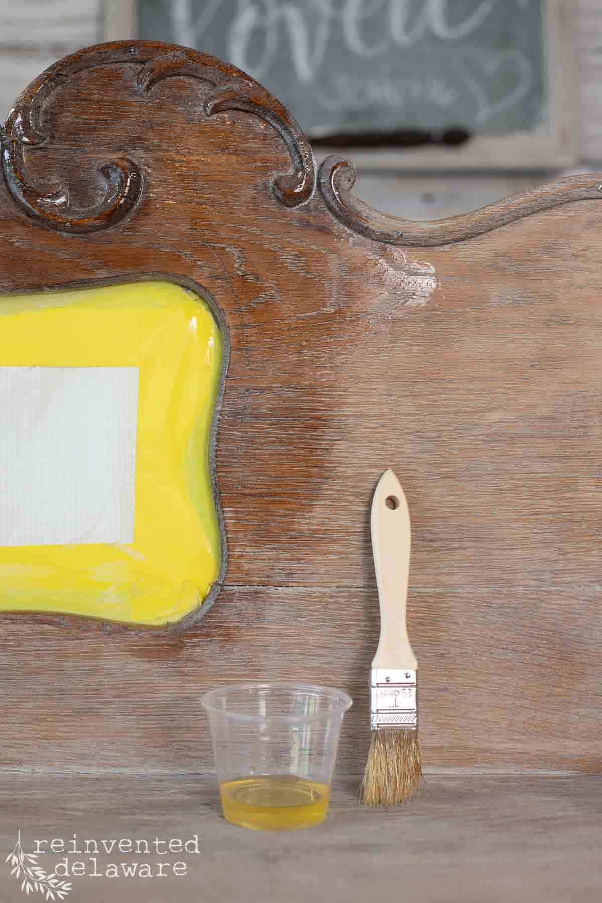 A cup of hemp oil and a chip brush used to seal old wood furniture makeovers.