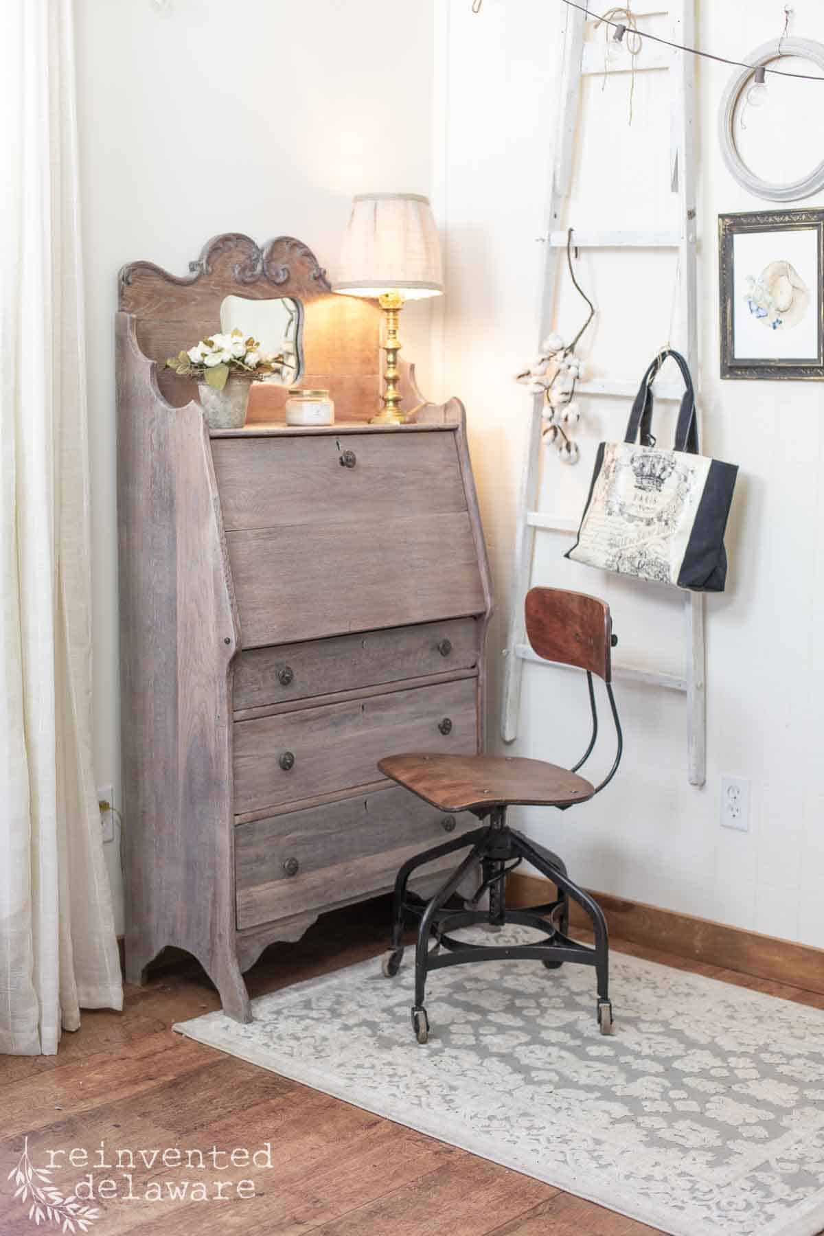 After shot of staged and whitewashed furniture makeover on an antqiue secretary desk that is solid oak. Staged with flowers, and old office chair.