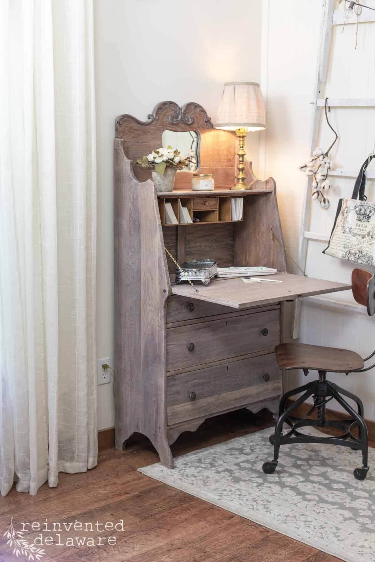 Antique fold-down secretary desk after a furniture makeover using a whitewashing technique and staged with home decor pieces and a lamp.