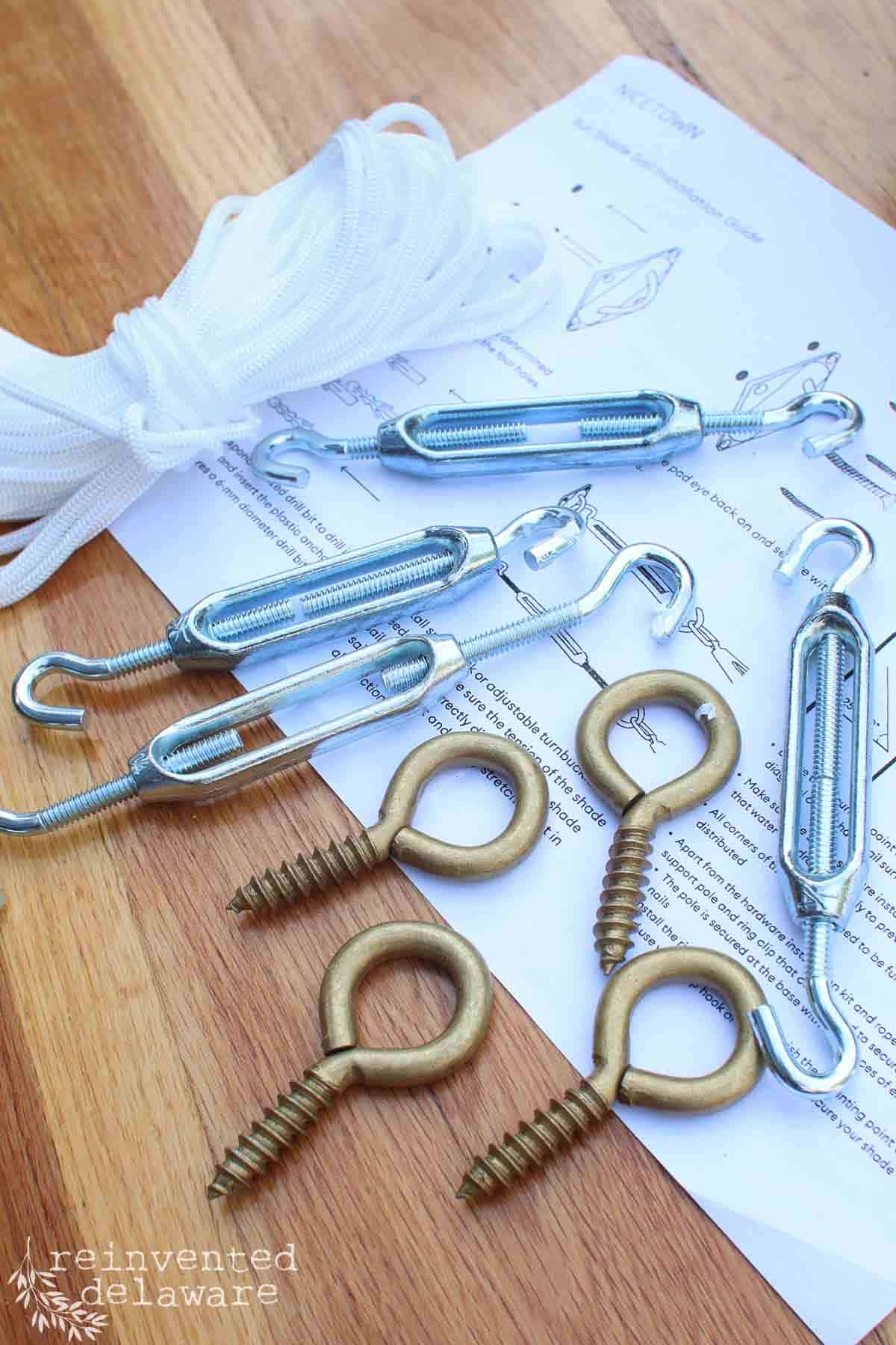 Hardware used to secure a sun shade sail to a wood pergola including eye bolts, turnbuckle and rope.