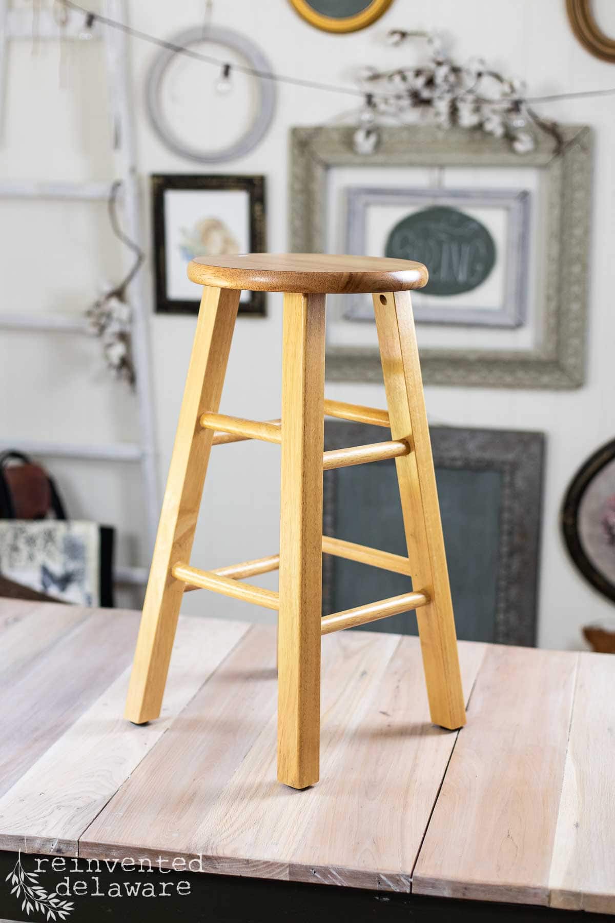 Thrift store wood stool sitting on top of a large craft table ready for a furniture makever.