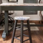 A wood bar stool that has been made over for a craft room using brown chalk paint and a furniture transfer in a vintage pattern.