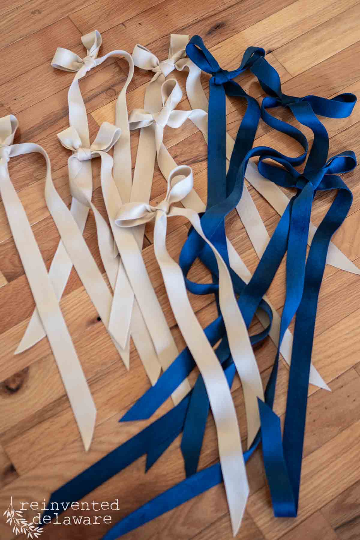 Beige and blue velvet ribbons tied in bows are laid out on a wooden floor.