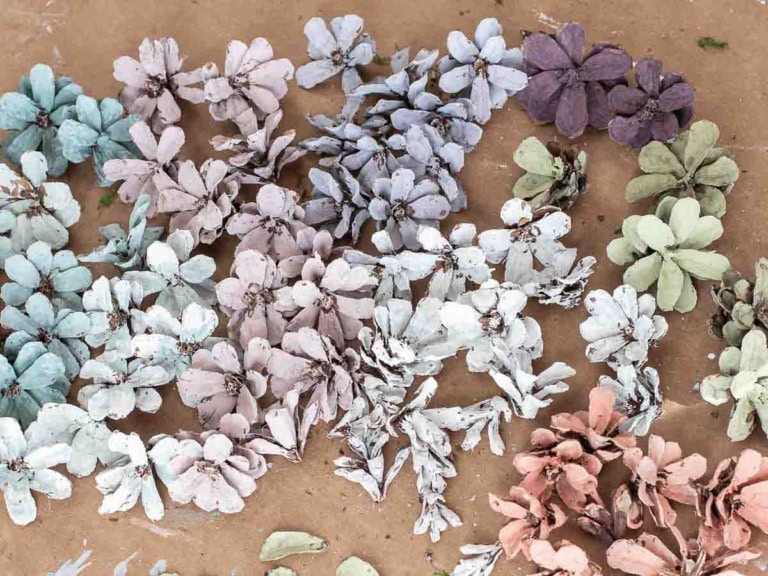 A variety of pastel-colored paper flowers, perfect for Easter decorations, including shades of blue, purple, green, and pink, are scattered on a brown surface—great for DIY ideas.