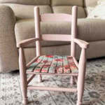 A thrift flip chair makeover: this small pink wooden chair with a floral-patterned woven seat sits on a patterned rug, in front of a beige sofa in a cozy living room.