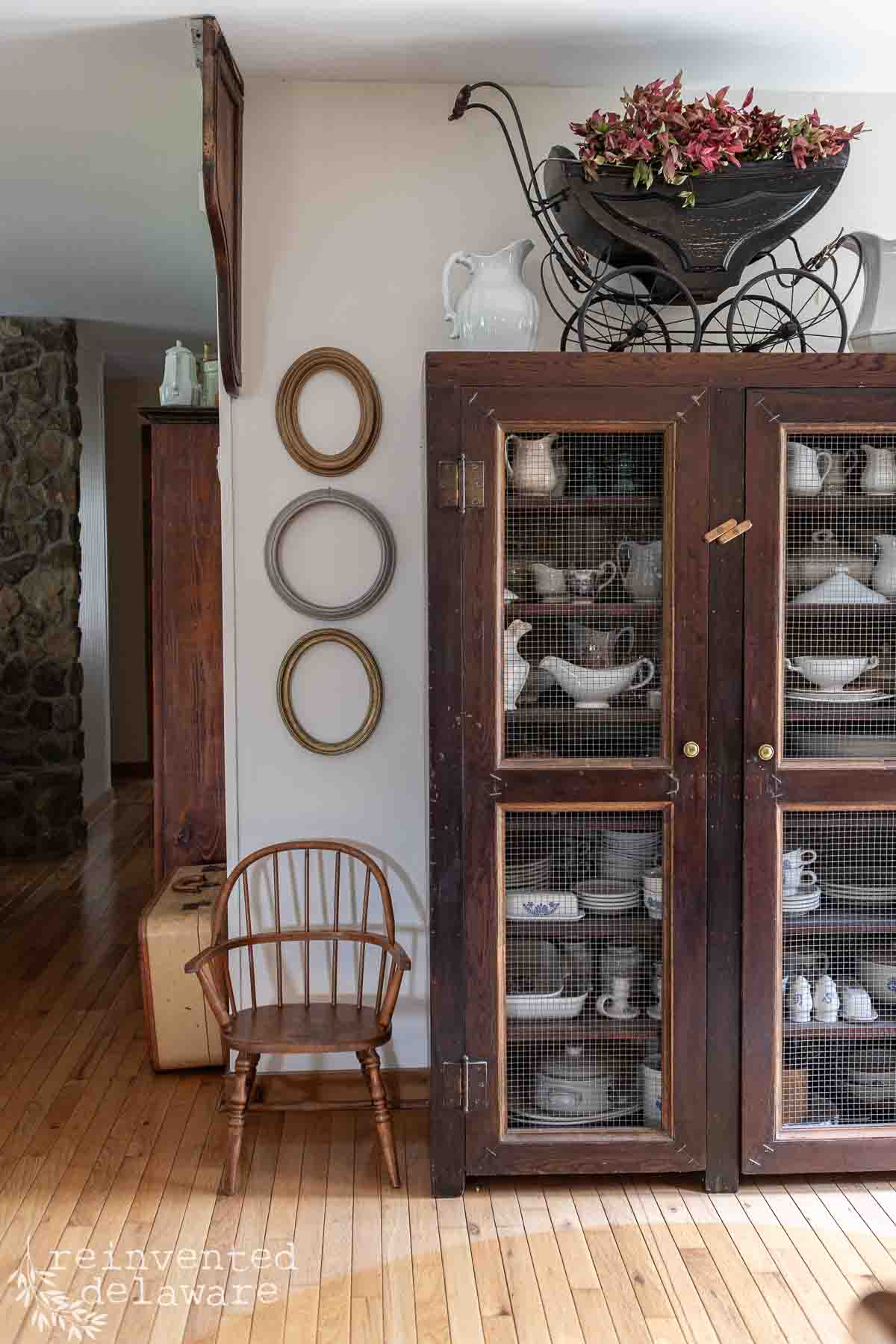 Vintage wooden cabinet with glass doors showcasing white dishware and kitchen accessories.
