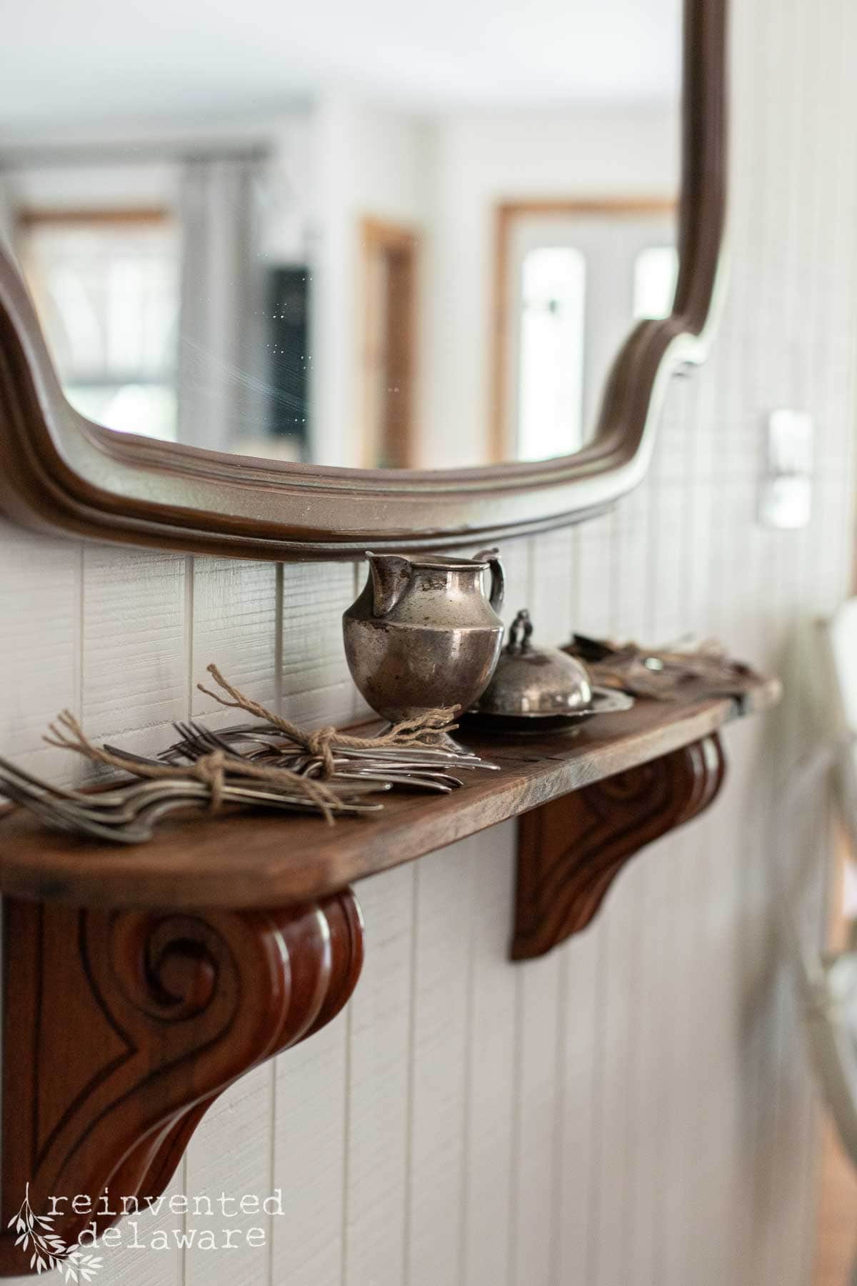 Vintage silverware and decorative items on a wooden shelf with a mirror.
