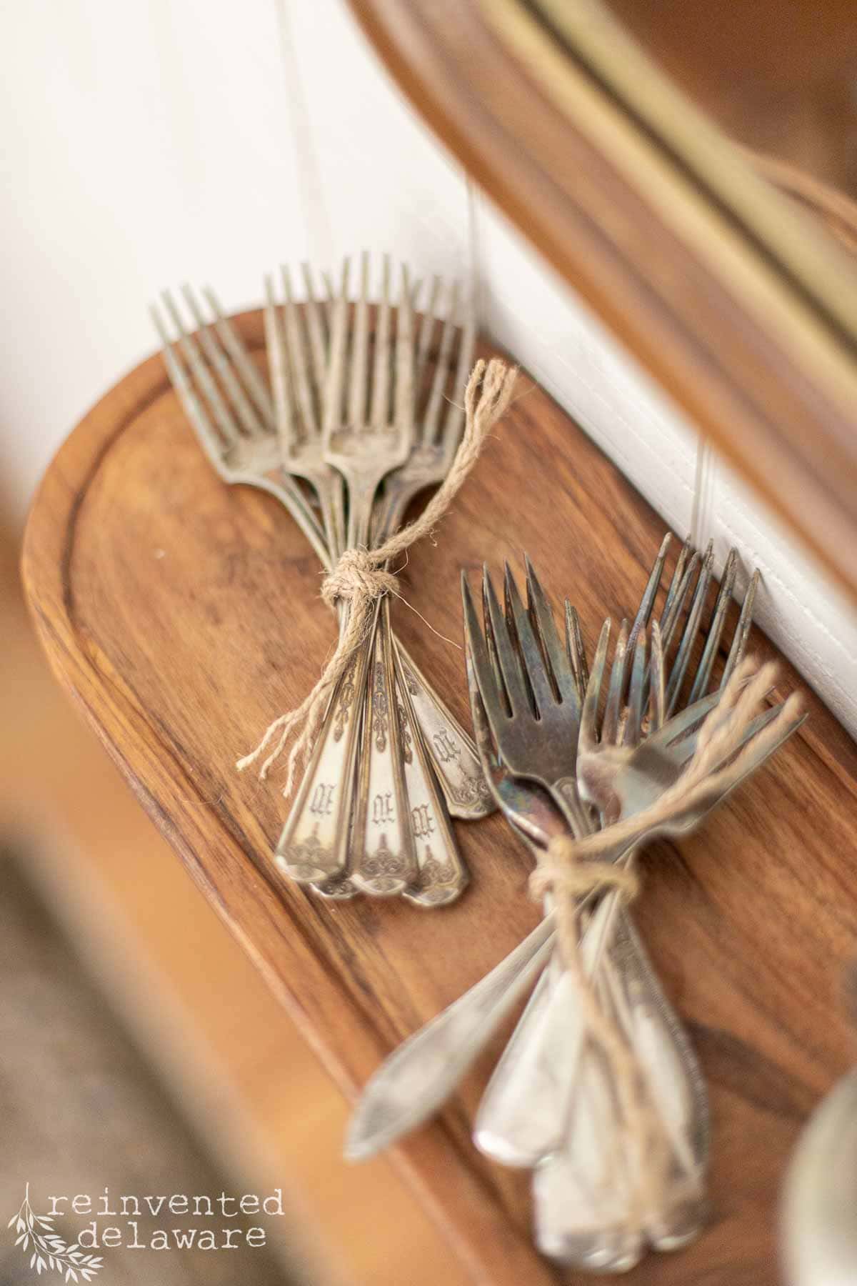 Vintage silver forks tied with twine on a wooden tray, showcasing rustic tableware.