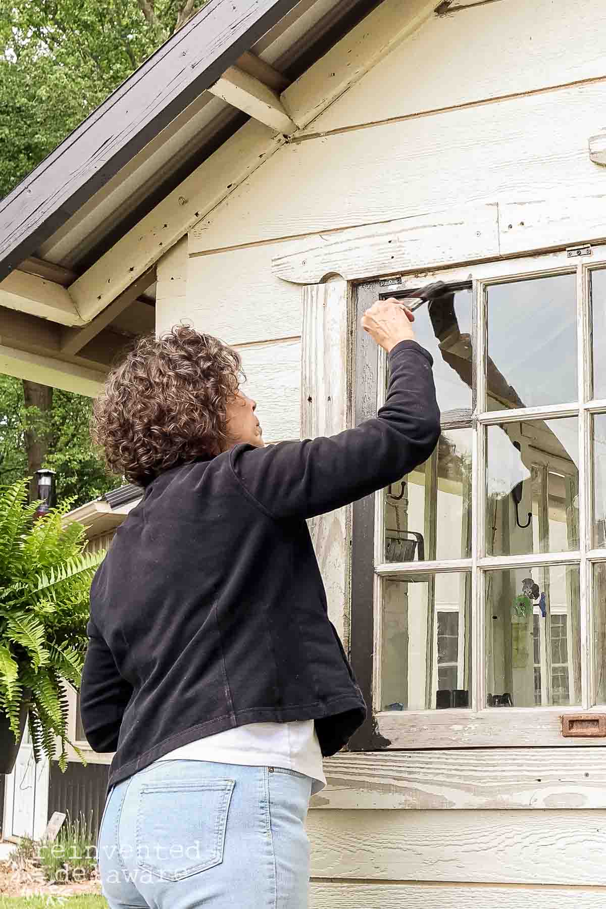 Woman painting a window on a rustic garden shed.
