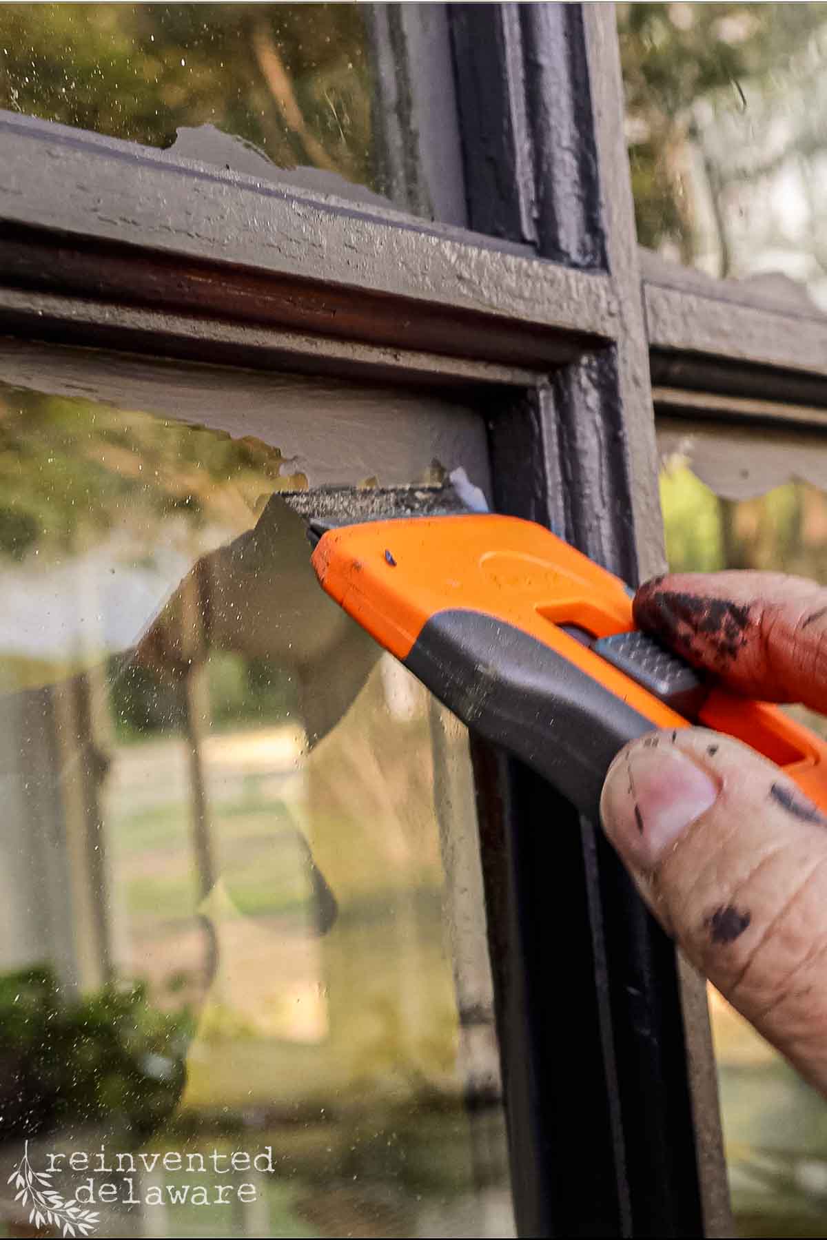 Hand using utility knife to remove old paint from window frame on she shed.